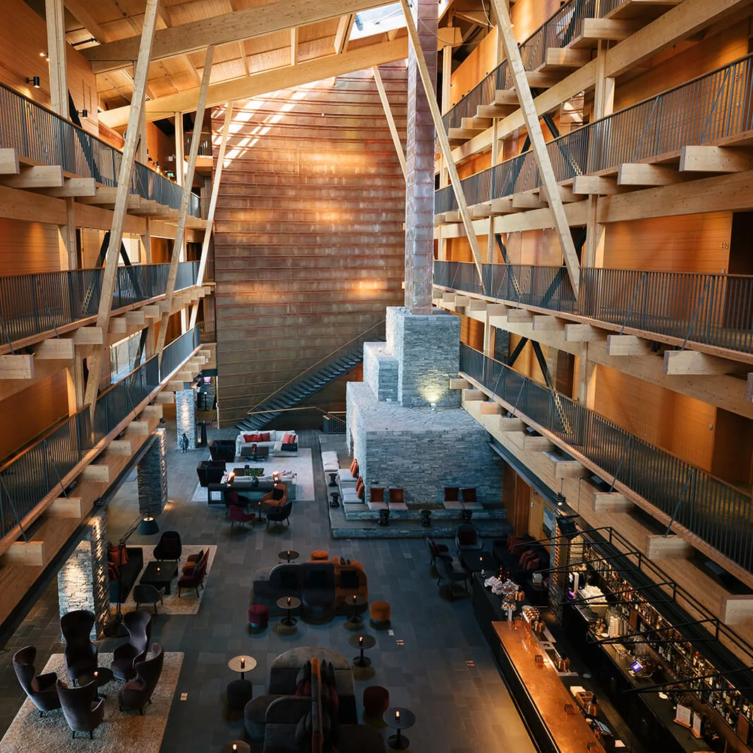 A multi-level wooden interior with crisscrossing staircases and seating areas, illuminated by ample natural light.