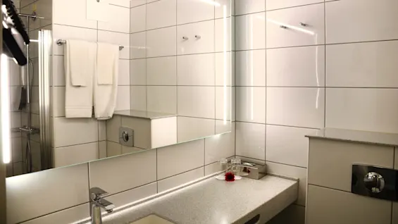 Et moderne bad rom med reflekterende overflater, opplyst speil, servanter, håndklær, og flislagte vegger.