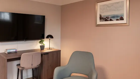 An inviting hotel room setup with a large TV, a functional desk area, and a plush armchair for unwinding.
