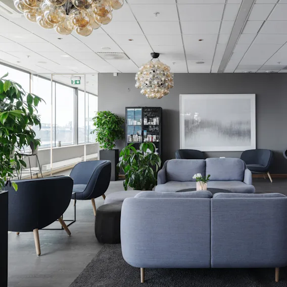 Bekväm sittgrupp med moderna grå soffor och stolar. Krukväxter och sfäriska ljuskronor tillför elegans, medan stora fönster ger naturligt ljus.