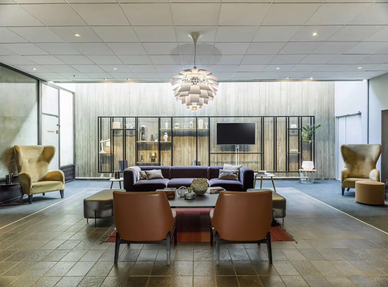 Moderne og koselig hotellobby med stilfulle lenestoler, en mørk sofa og en iøynefallende taklampe.