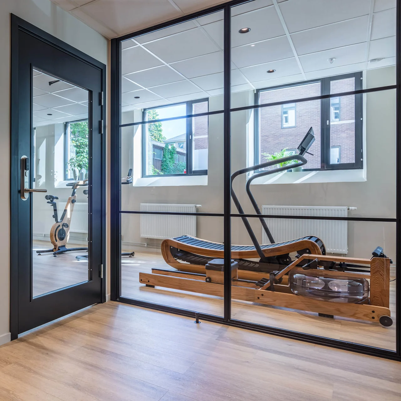 Glass doors lead to a modern gym with exercise equipment, wooden floors, and natural light.