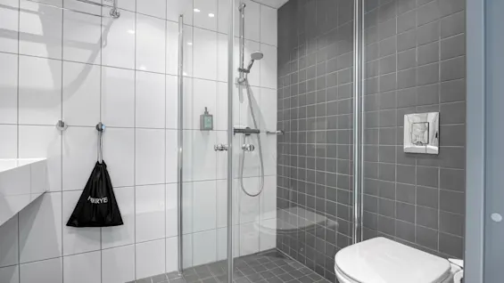 Et moderne bad med dusj, toalett og en svart pose med teksten HRYE hengende på en krok.