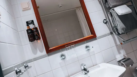 Et bad med et speil med treramme, et krom håndklestativ med sammenlagte håndklær og to såpedispensere på veggen. Tekst på såpen lyder: "TAKE ME! ENJOY! Relax. Rituals."