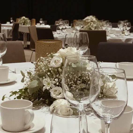 En formell spisesal dekket for et arrangement, med bord pyntet med hvite duker, elegante glass og blomsteroppsatser.