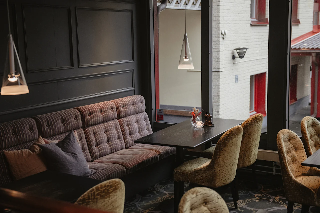 A cozy dining area at Home Hotel Kung Oscar with a long booth, tables, and chairs, perfect for a relaxing meal or conversation.