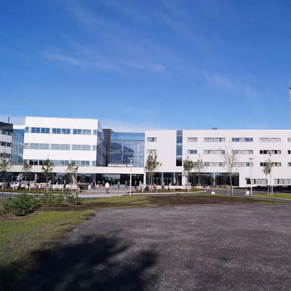 En stor, moderne hotellbygning med teksten "Quality Hotel Expo", omgitt av noen mennesker som går på en betonggangvei, mot en klar blå himmel.