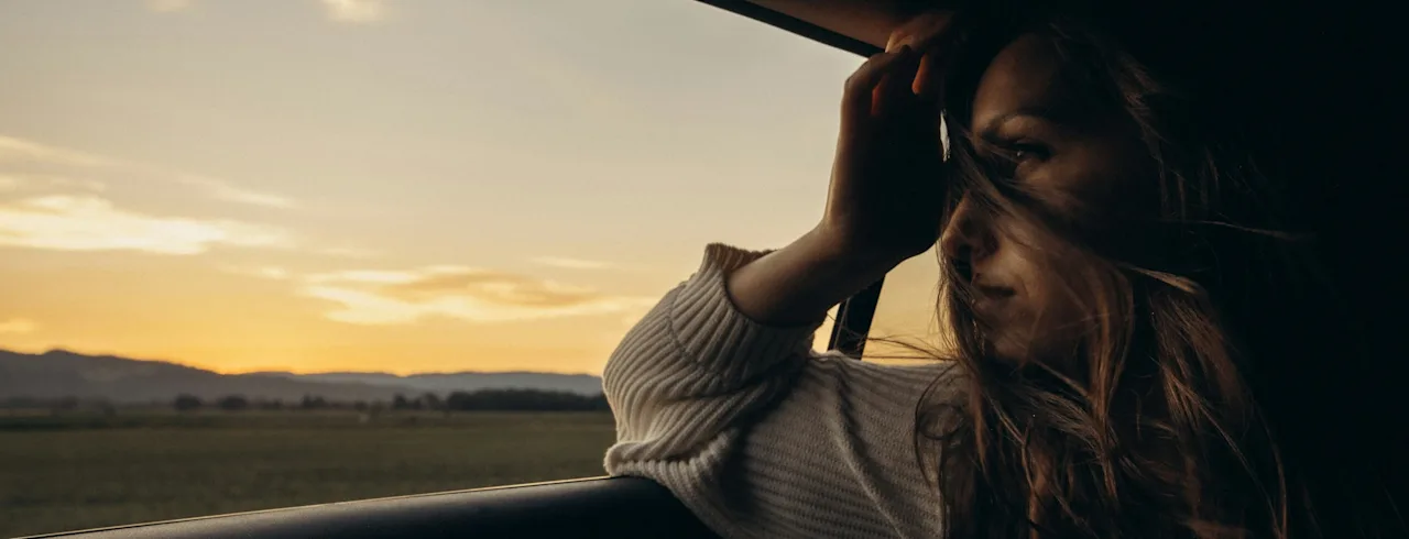 Njuter av en naturskön bilresa i solnedgången, med håret som blåser lätt i vinden.