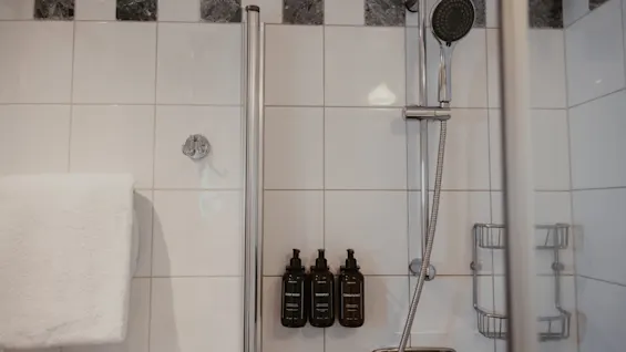 En ren bruser med hvide fliser, et brusehoved og tre flasker mærket Body Wash, Shampoo og Conditioner.