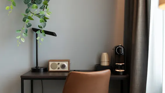 En koselig skrivebordsplass med en plante, en moderne lampe, en radio i vintagestil og en kaffemaskin, ved siden av en komfortabel stol.