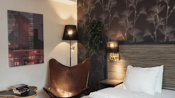 Viihtyisä hotellihuone sängyllä, lukuistuimella ja lämpimällä valaistuksella, täydellinen rentoutumiseen.