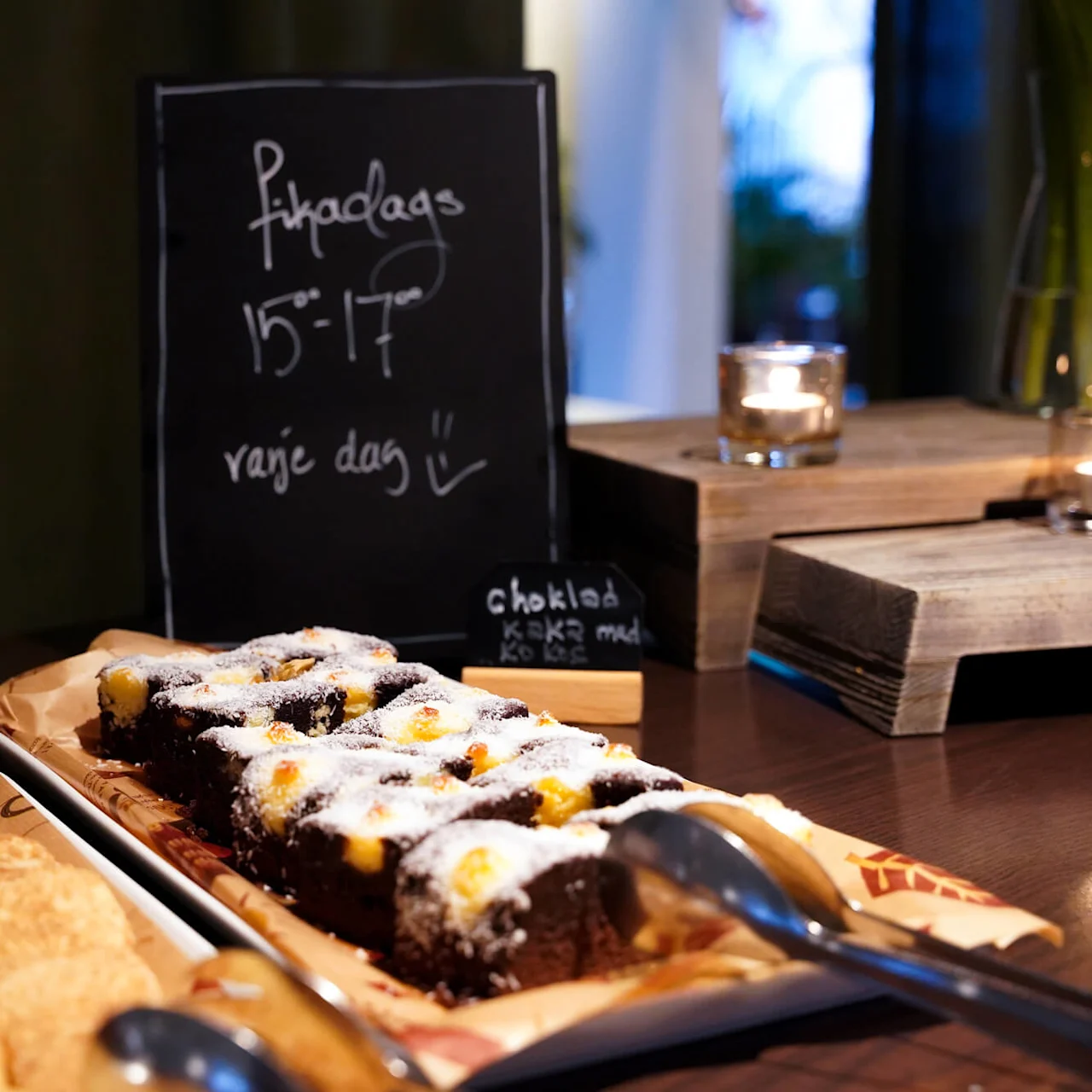Cookies and brownies on a cafe counter with a blackboard displaying "Fikadags varje dag".