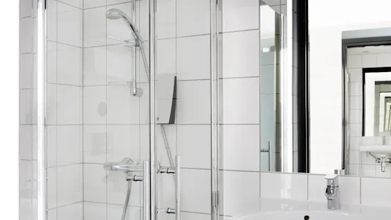 A modern shower and sink in a clean white-tiled bathroom.