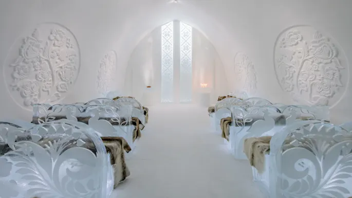Elegante isbenker pyntet med intrikate utskjæringer står på rekke i et snøkapell. Myke pelser dekker setene. Gjennomgående mønstre pryder veggene, sammen med dempet belysning.