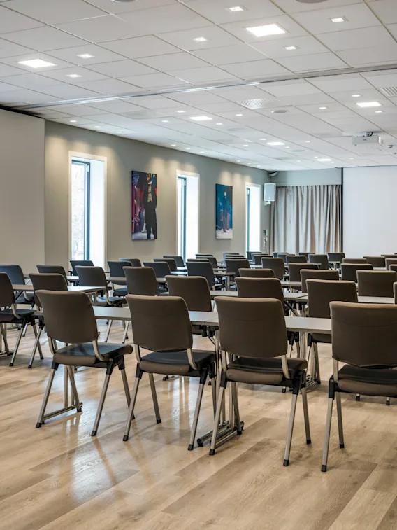 Et romslig, moderne konferanserom med rader av bord og stoler, klart for et møte eller en presentasjon.