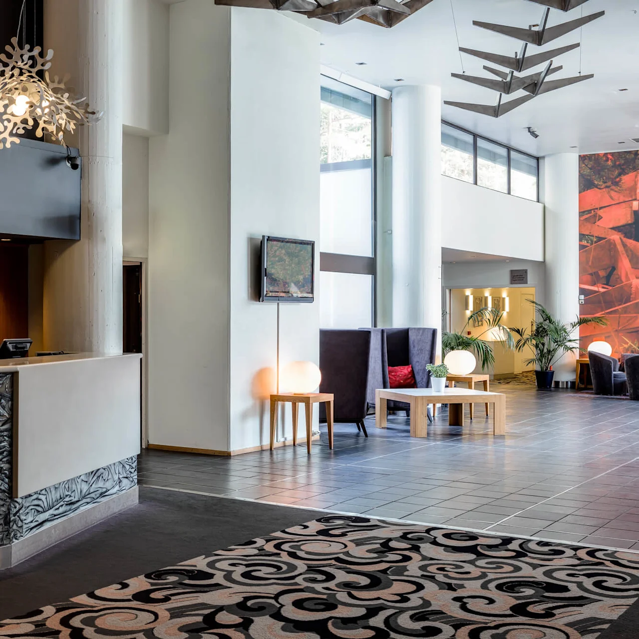 Reception desk displays "Quality Hotel Entry"; chandelier overhead; lobby with modern furniture, patterned carpet, and large windows; abstract wall art visible.