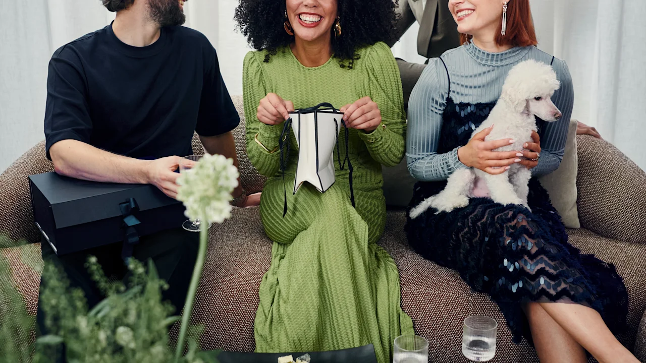 Venner nyter en livlig sammenkomst i en sofa, deler gaver og latter, med en liten hund og forfriskninger i nærheten.