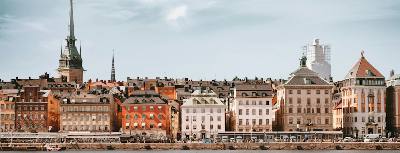 Smuk udsigt over historiske farverige bygninger og et kirkespir langs Stockholms havnefront.