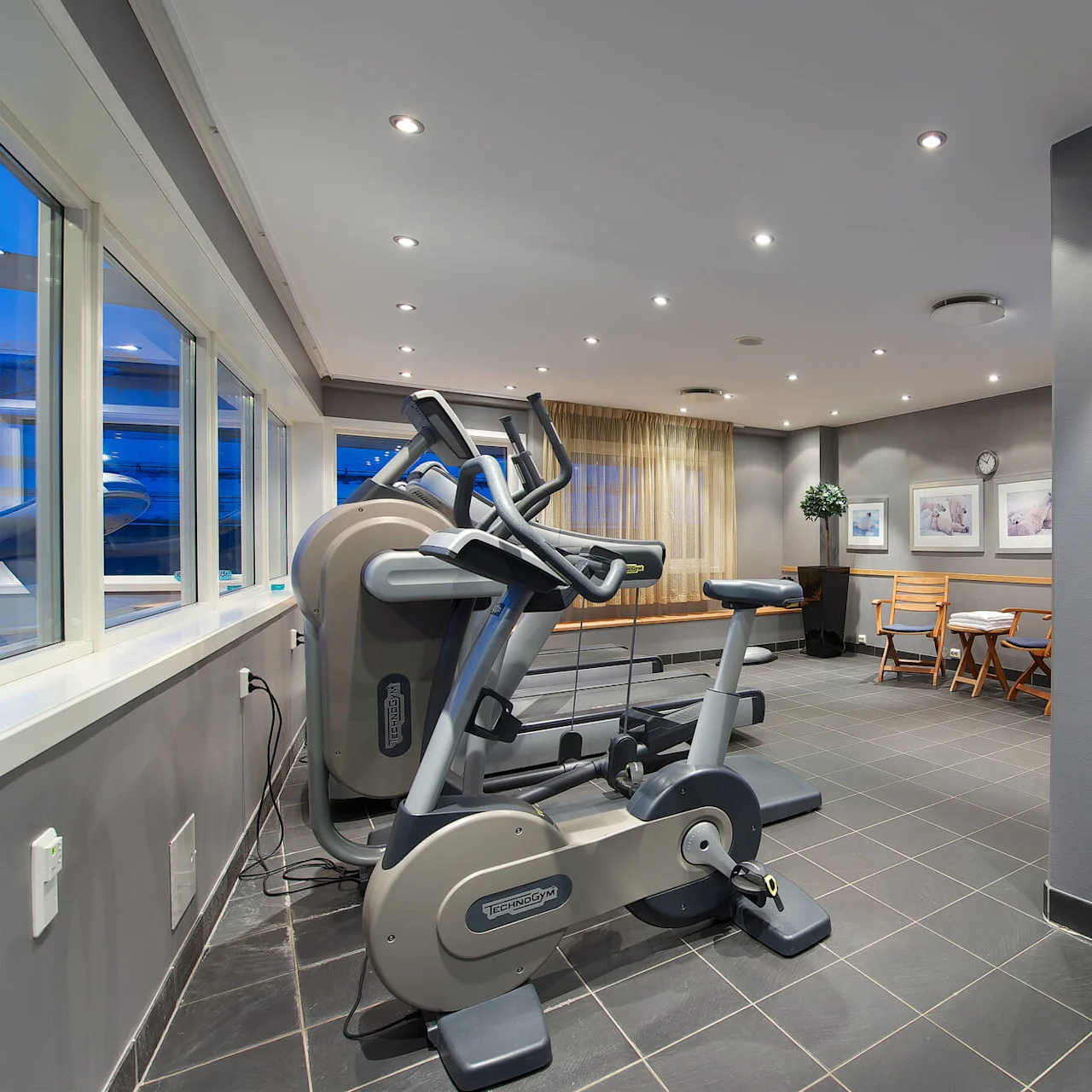 Exercise bike positioned near window in a clean, well-lit indoor gym with seating area and television in the background.
