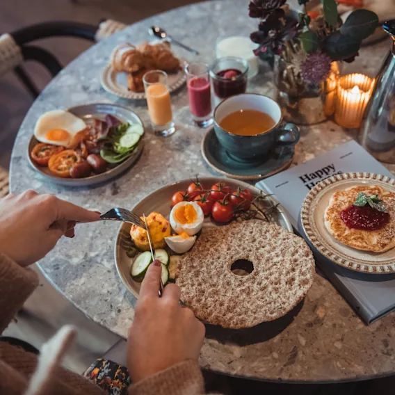 Bilde ovenfra av et frokostbord på hotellet med knekkebrød, kokt egg, pannekaker, speilegg med bacon, te og juiceshots.