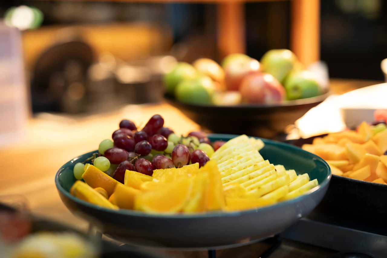 En farverig udstilling af frisk frugt, herunder druer, appelsinskiver og ananas, arrangeret i en skål.