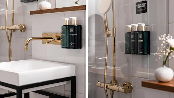 Ett modernt badrum med gyllene detaljer och väggmonterade tvålpumpar vid en handfat och dusch för en ren och elegant känsla.