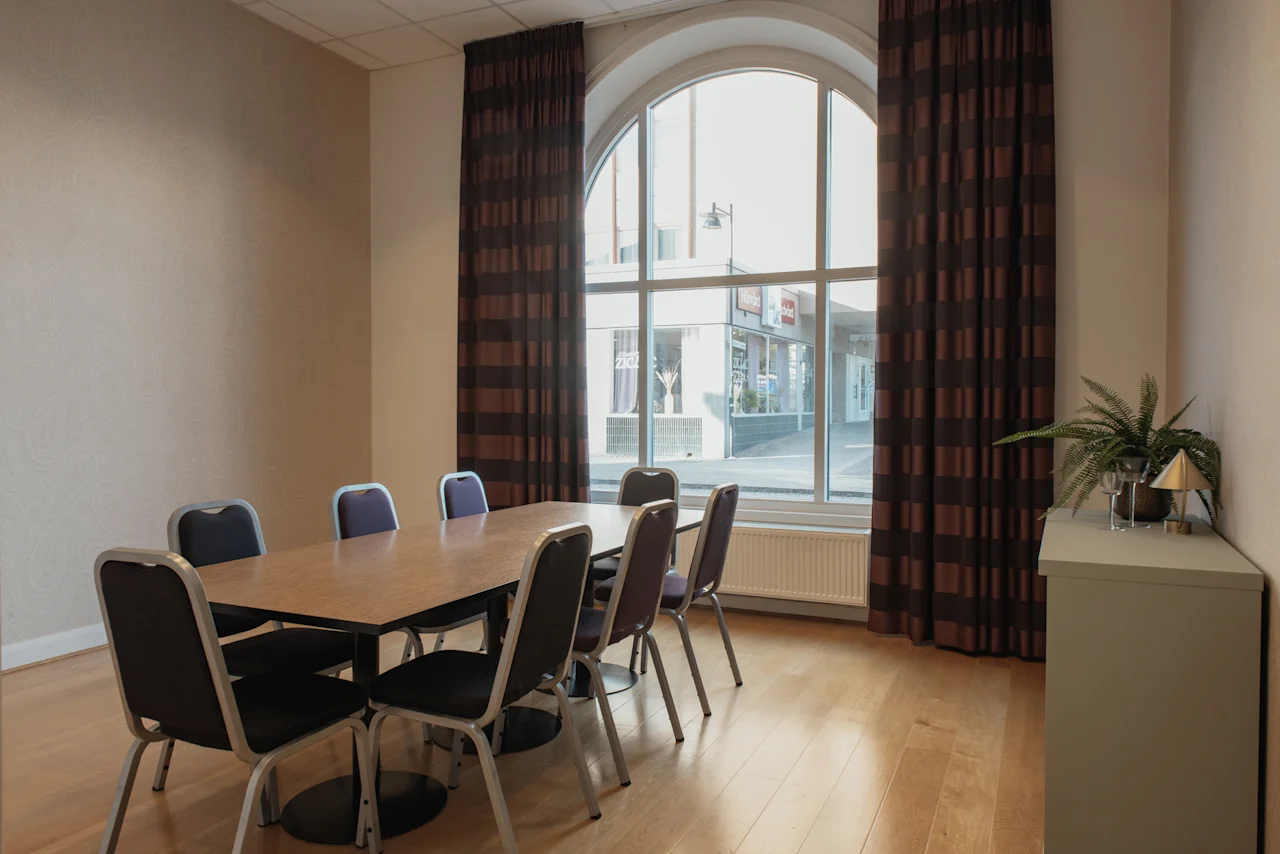 Ett ljust mötesrum med ett långt bord och stolar, med ett stort välvt fönster som vetter mot en gatuscen.