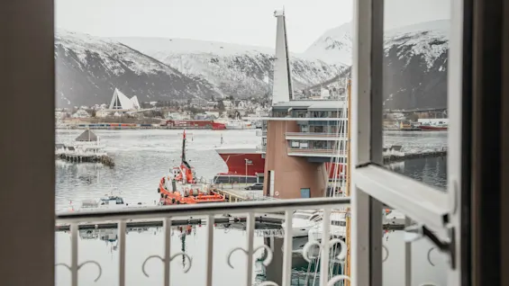 View from a balcony overlooking a harbor with a boat and snow-capped mountains in the background.