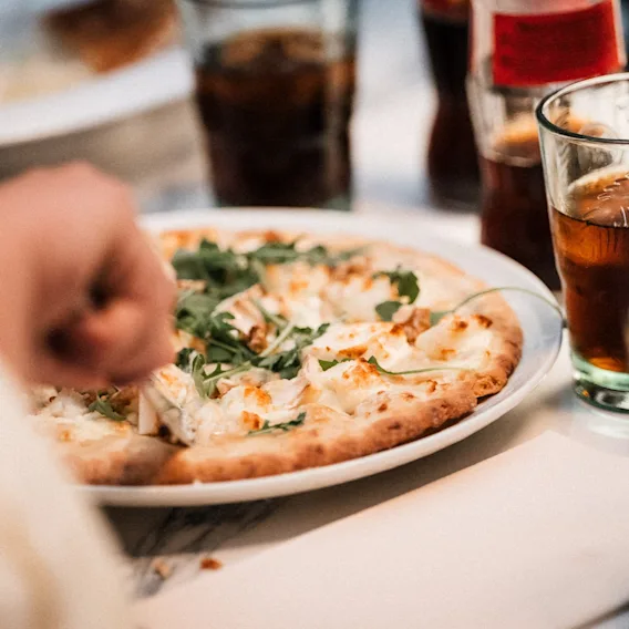 Nyt et måltid med pizza toppet med ost og grønt, akkompagnert av forfriskende drikker.