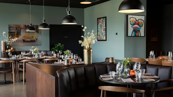 A stylish restaurant interior with set tables, comfortable booths, and modern artwork on the walls, creating a cozy dining atmosphere.