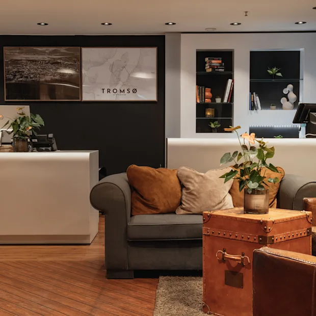 A welcoming hotel lobby featuring a reception desk and a cozy seating area, with 'TROMSO' displayed prominently on the wall.