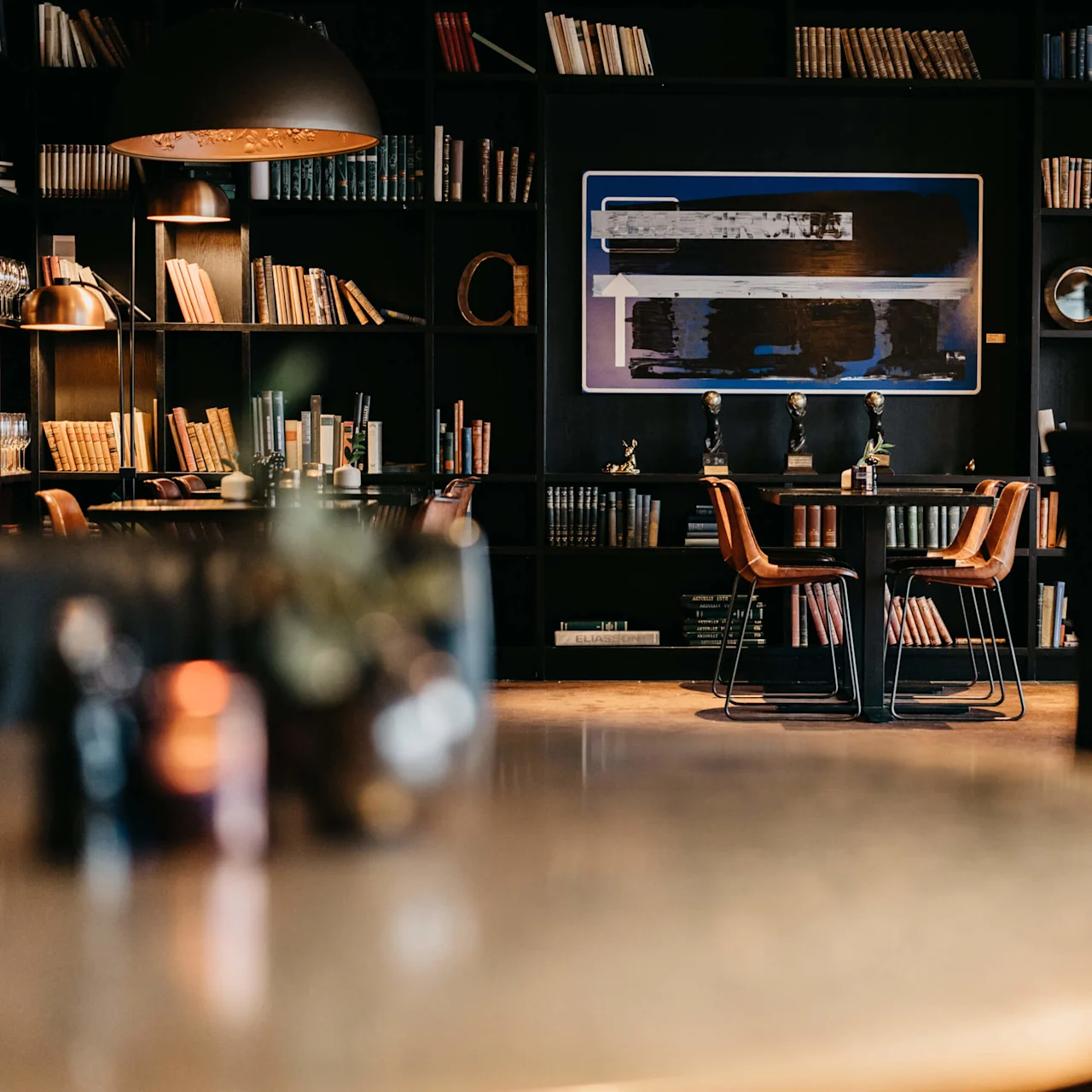Elegant library bar with leather stools, books, warm lighting, and shelves in a cozy, upscale setting.