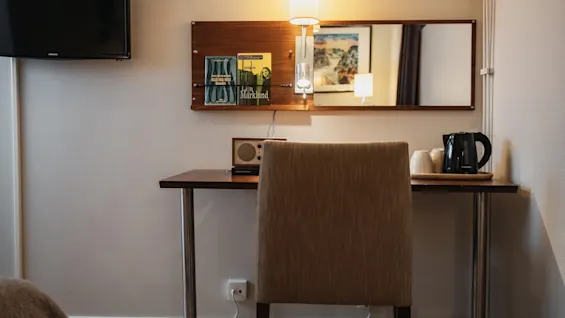 A hotel room desk area with a chair, magazines (ALLA JAG VART, Liva Marklund), and a kettle. Home Hotel Kung Oscar.