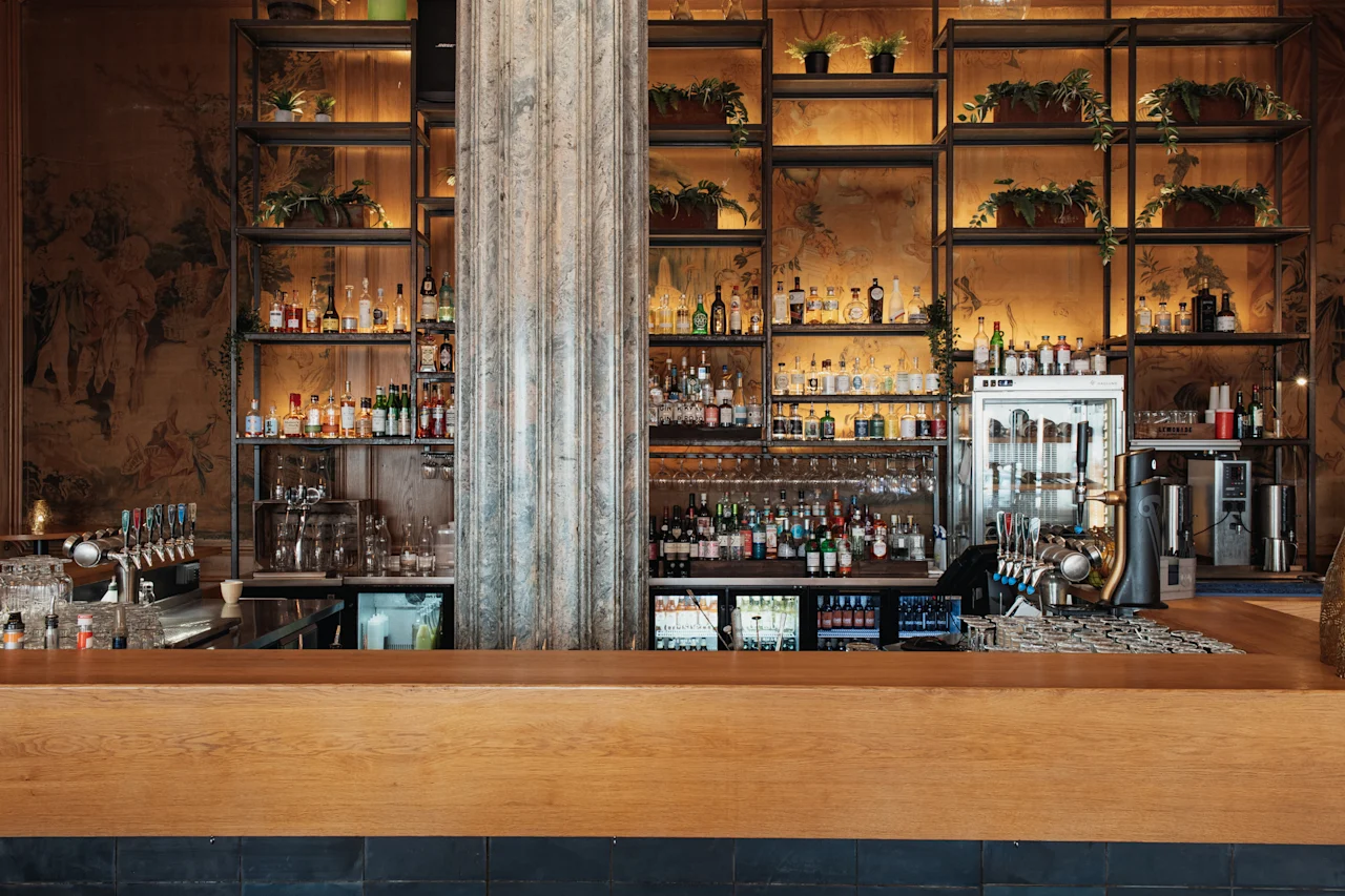 En stilren och välfylld bar på Home Hotel Grand, Helsingborg, med hyllor av flaskor, växter och bardiskar.