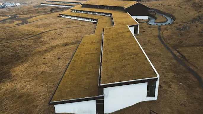 Moderne bygning med grønt tak strekker seg over karrig, kupert landskap og smelter inn i det jordlige miljøet under en overskyet himmel.