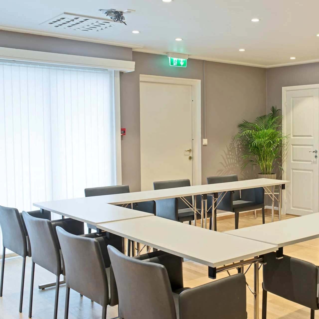 Et moderne konferanserom med oppsatte bord, stoler, en stor skjerm, og innendørs planter.