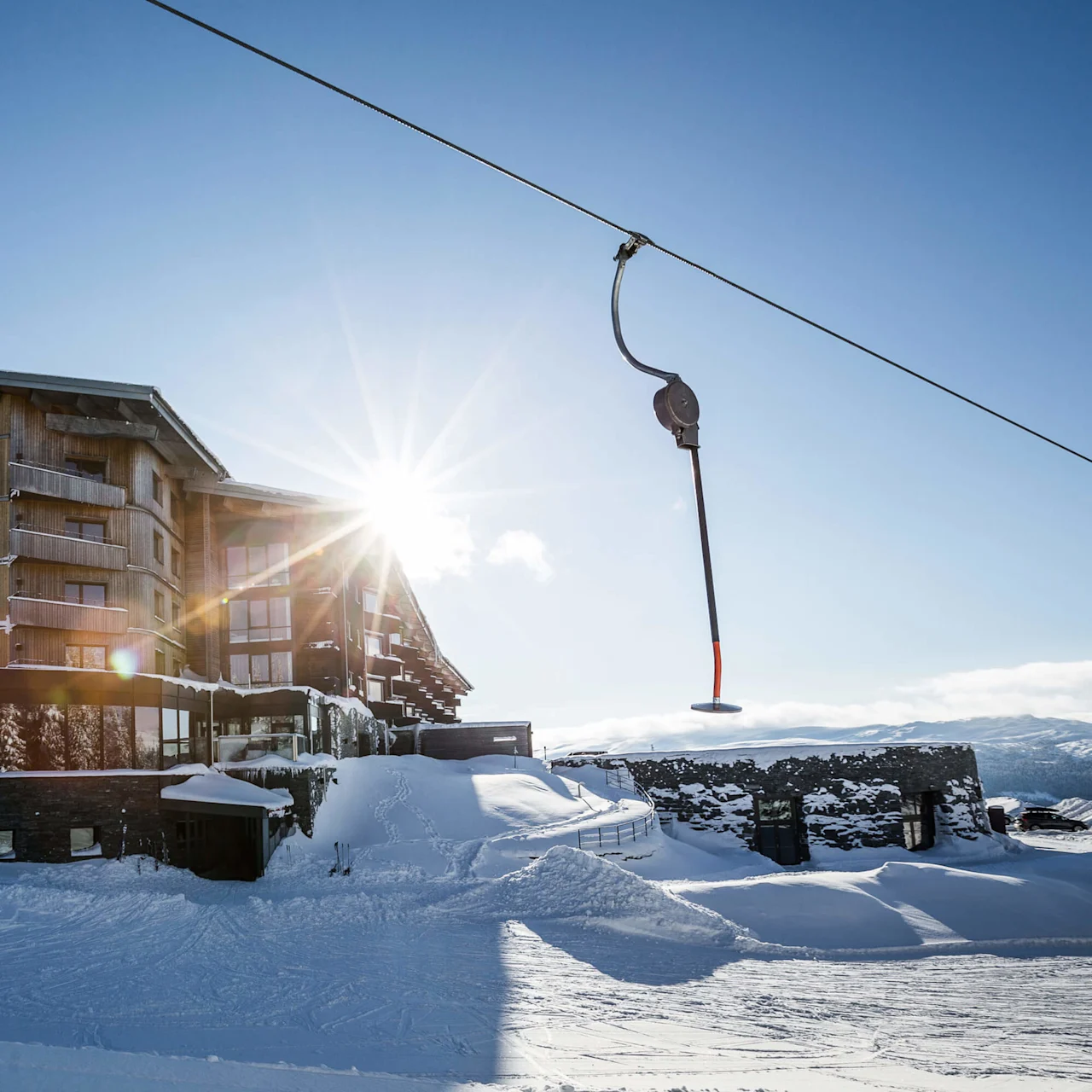 A modern ski resort building with a sunburst over snowy mountains.