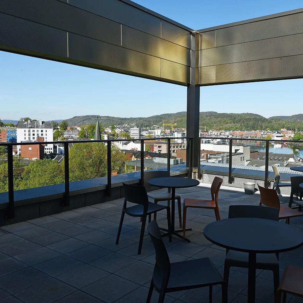 Borde og stole står på en tagterrasse med udsigt over et bylandskab med bakker og en flod under en klar himmel.