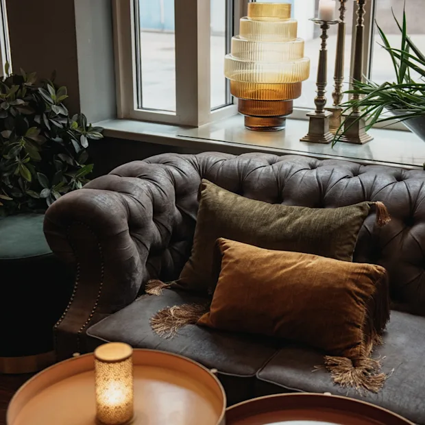 En bekväm och inbjudande loungeavdelning med en tuftad soffa med plyschkuddar, stämningsbelysning och frodig grönska.