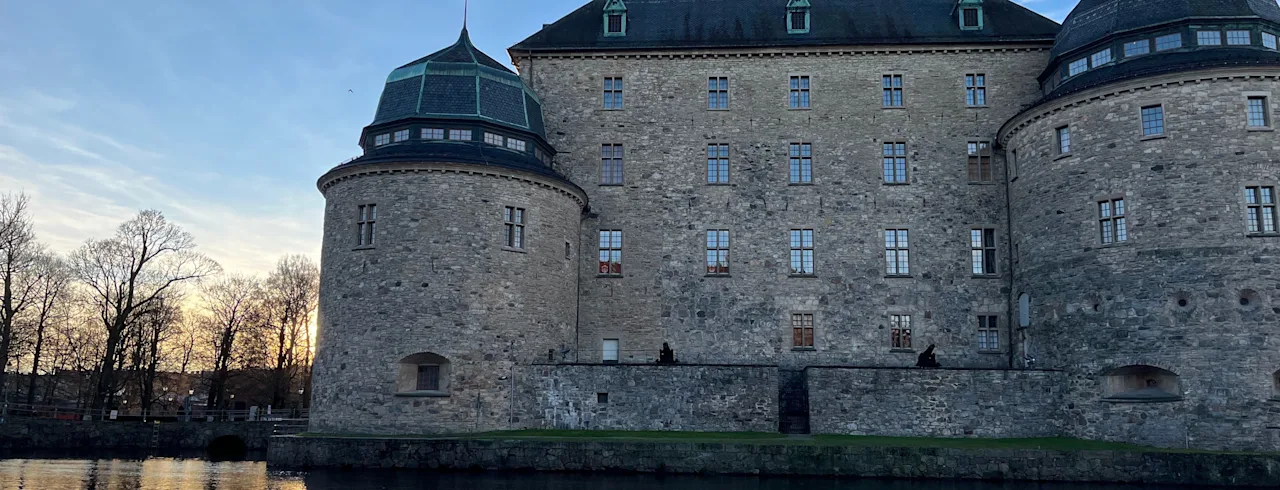 Örebro slott, et storslået stenslot med runde tårne, spejlet i roligt vand under en delvist skyet skumringshimmel.