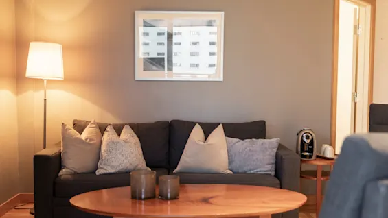 En koselig stue med en mørk sofa, dekorative puter, et salongbord i tre og en varm lampe, som skaper en innbydende atmosfære.