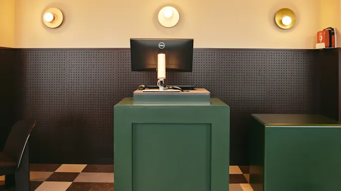 Det innbydende resepsjonsområdet på Stopover Hotel Falkenberg, med stilige grønne disker, en datamaskin og et særegent rutete gulv.