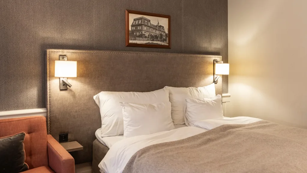 A comfortable and inviting hotel room at Home Hotel Grand Bodø, featuring a large bed with soft linens and warm lighting.