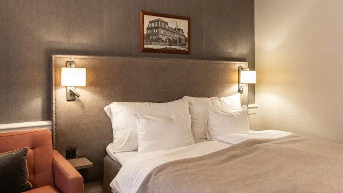 A comfortable and inviting hotel room at Home Hotel Grand Bodø, featuring a large bed with soft linens and warm lighting.