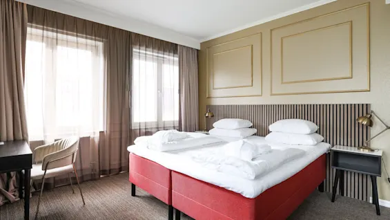 Viihtyisä hotellihuone Comfort Hotel Linköping Cityssä kahdella sängyllä, työpöydällä ja lämpimällä valaistuksella.