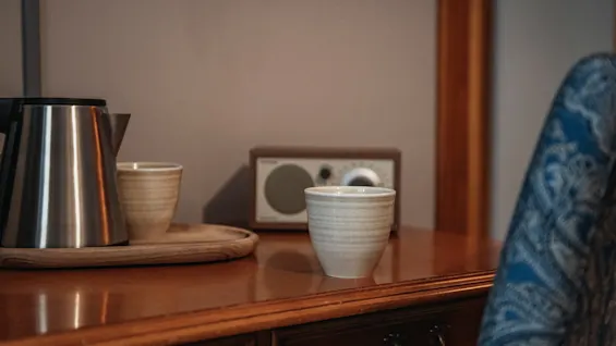 Vattenkokare och koppar på en träbricka med en radio i bakgrunden, vilket antyder en avkopplande stund.