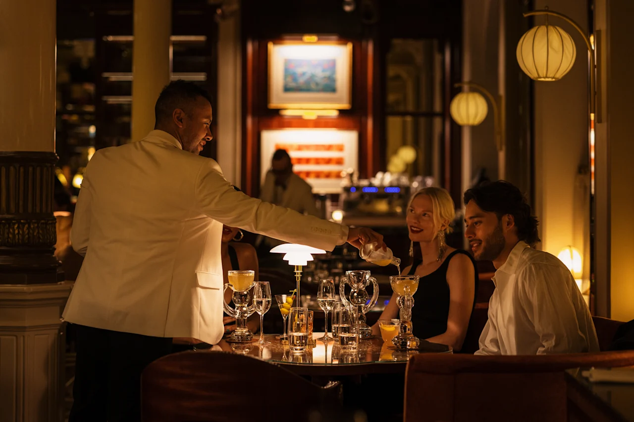 Tarjoilija kaataa juomaa vieraille Hotel Kämp – Kämp Barissa, luoden elegantin ja sosiaalisen tunnelman.