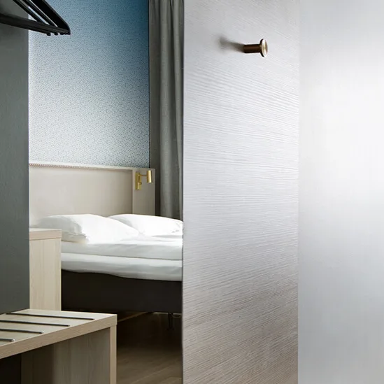 A modern, minimalistic hotel room split by an open door; two twin beds, soft lighting, wall-mounted TV, and curtains in a cozy ambiance.