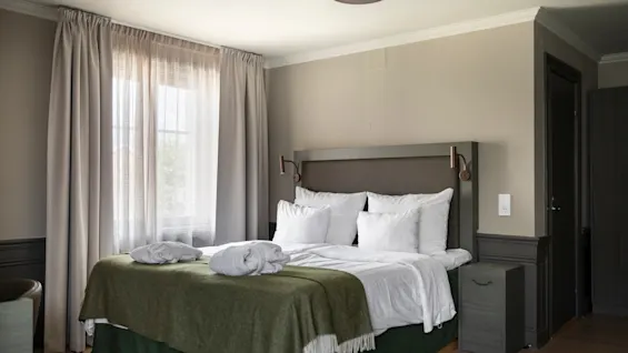 Kutsuva hotellihuone, jossa on mukava sänky, raikkaat valkoiset liinavaatteet, vihreä peitto ja kaksi pehmeää kylpytakkia.