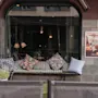 Kutsuva ulkoistuinalue, jossa on kuvioituja tyynyjä penkillä, suurten ikkunoiden ja kahden mainosjulisteen kehystämänä: Händer på Plaza ja Bubbelifredag!